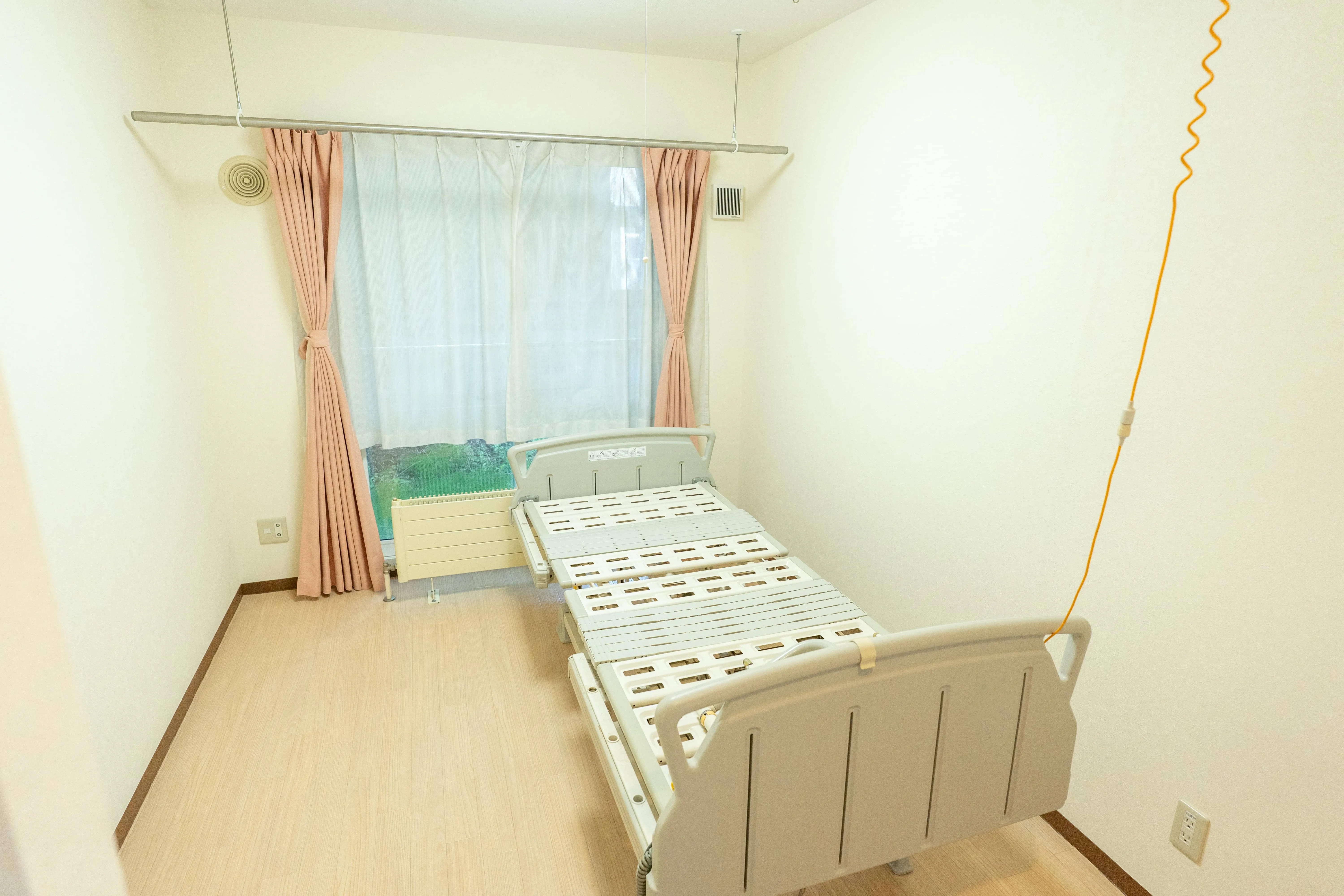 介護施設の居室。ベッドと窓、カーテンが備えられた個室